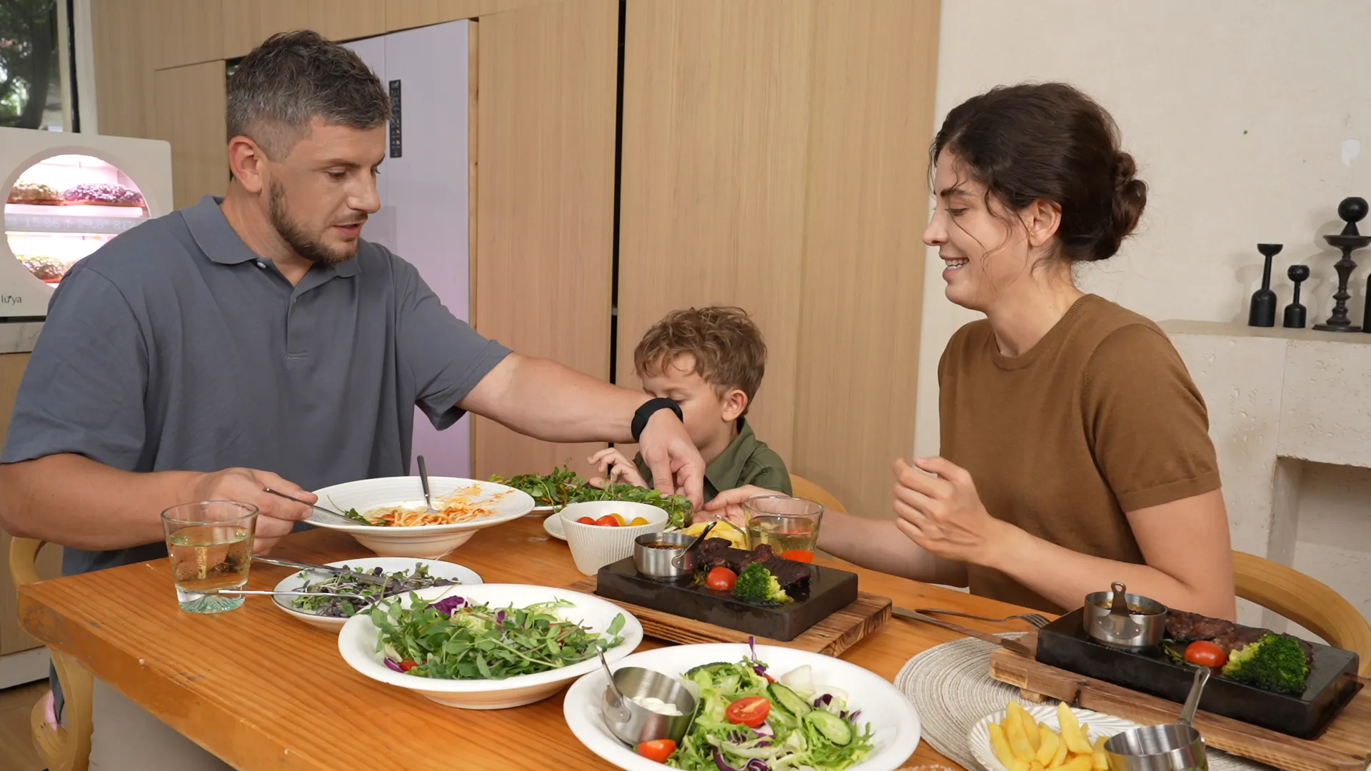 A family at the kitchen table, the mother serving freshly cut microgreens onto a child's plate
