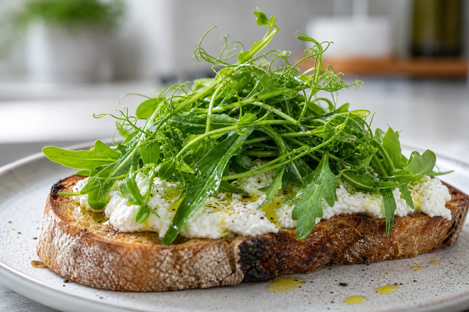 A close-up of ricotta toast topped with bright green pea shoots and arugula microgreens